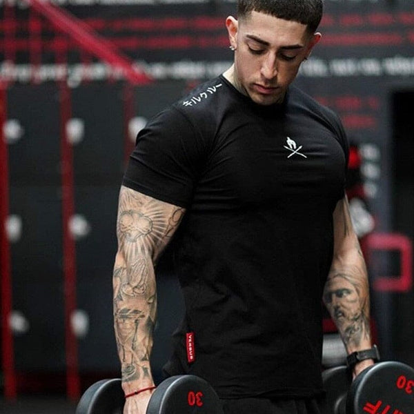 Atleta com braços tatuados usando a camiseta preta Spartan para treino de musculação com halteres.