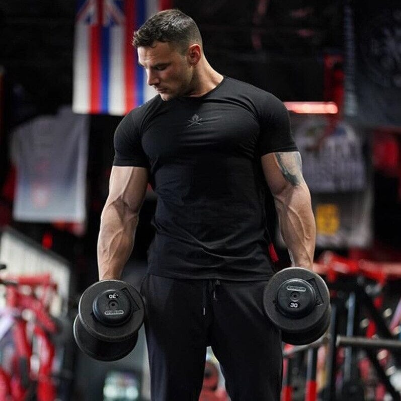 Atleta com camiseta preta Spartan da Iron Club se preparando para levantar halteres pesados na academia.