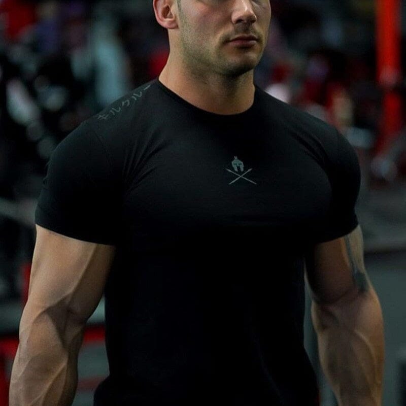 Close-up do caimento slim fit da camiseta Spartan preta no corpo de um atleta, destacando o peito e os braços.